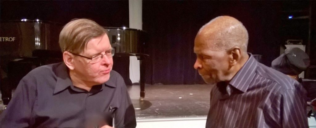 A white man with glasses and a black man seated together in conversation
