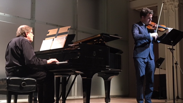 A man playing piano and a man playing violin on a stage